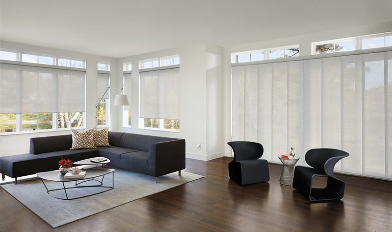A modern living room with a dark sectional, black accent chairs, and floor-to-ceiling windows featuring white blinds.