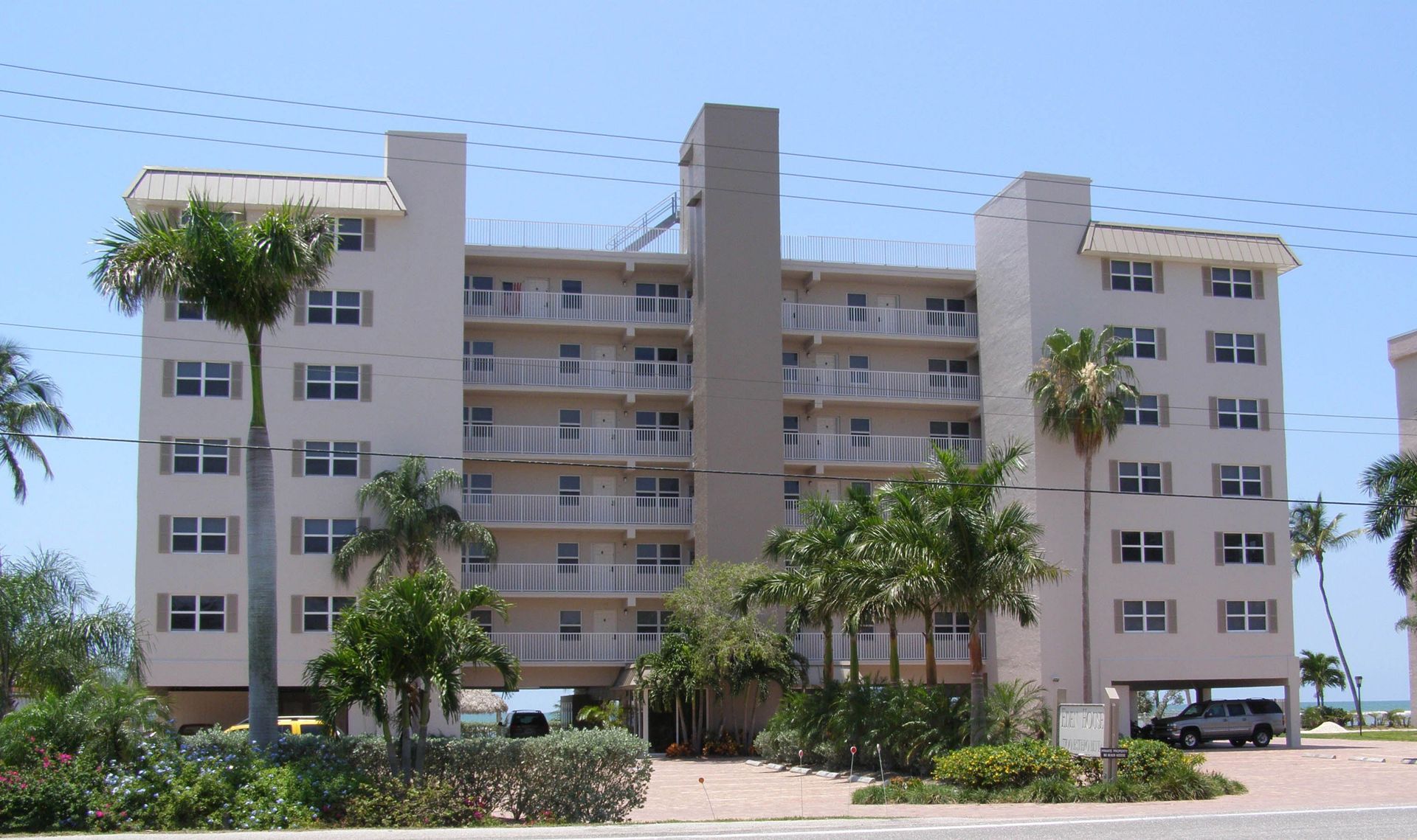 A five-story, beige apartment building surrounded by palm trees and landscaping under a clear blue sky.
