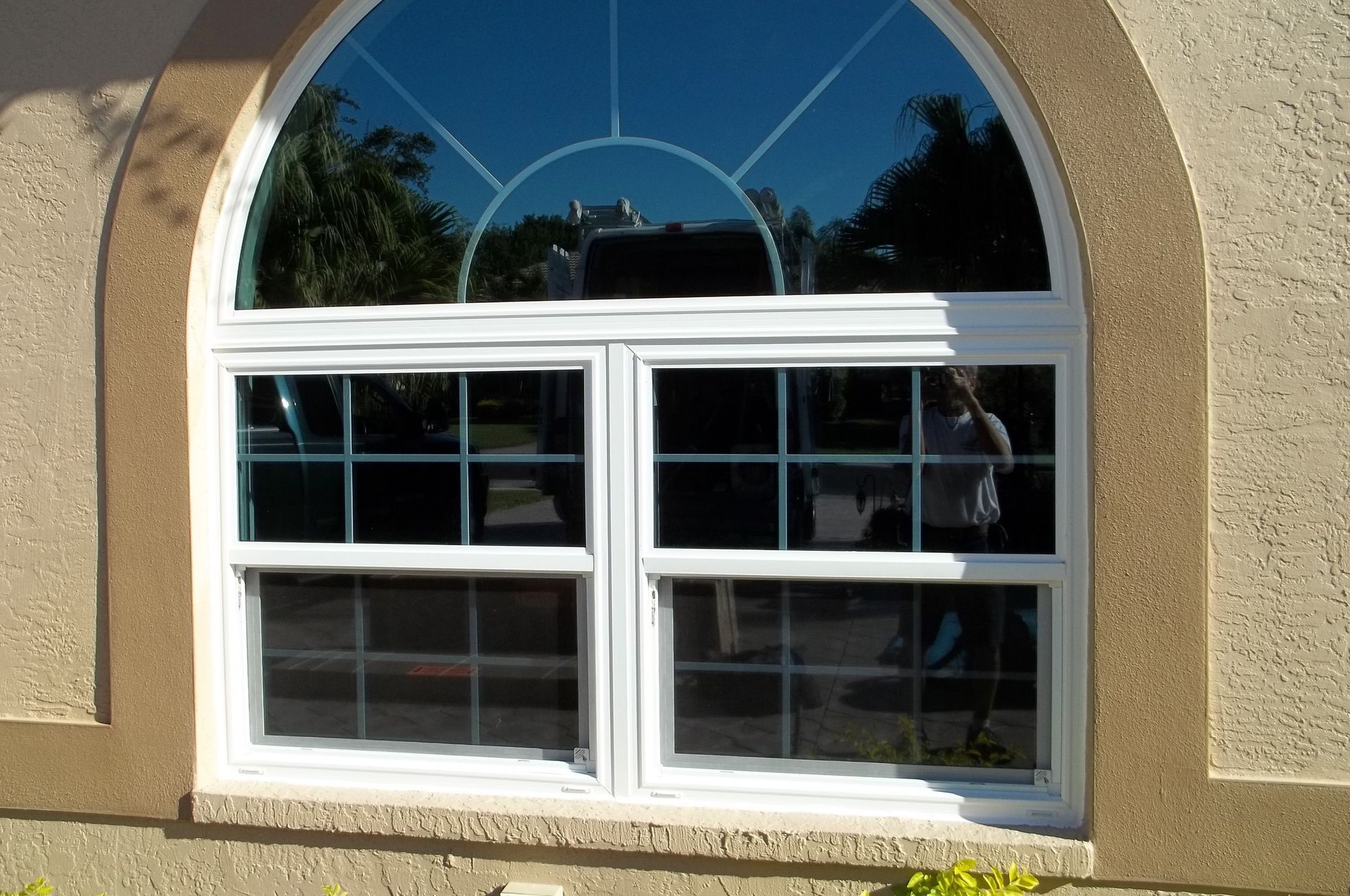 A white-framed arched window with colonial grids and a fanlight top, set in a beige, textured stucco wall.