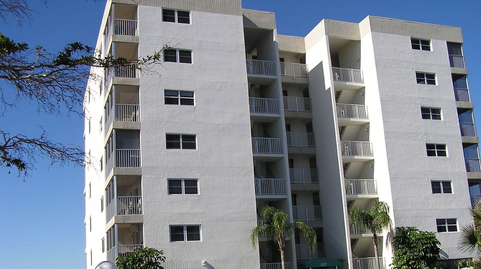 A tall, multi-story white apartment building with balconies, set against a clear blue sky.