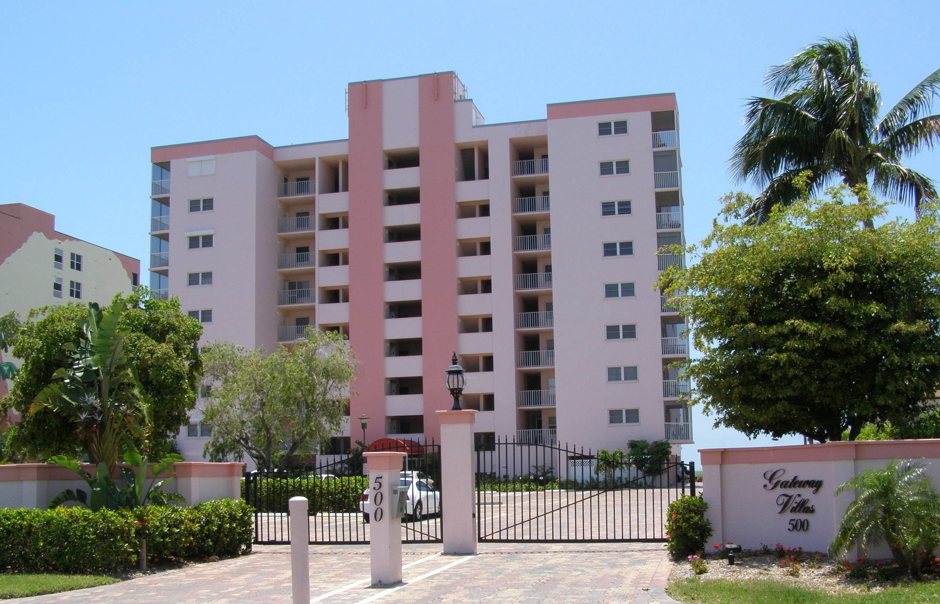 A pink-and-white high-rise residential building behind a metal gated entrance with a sign reading 