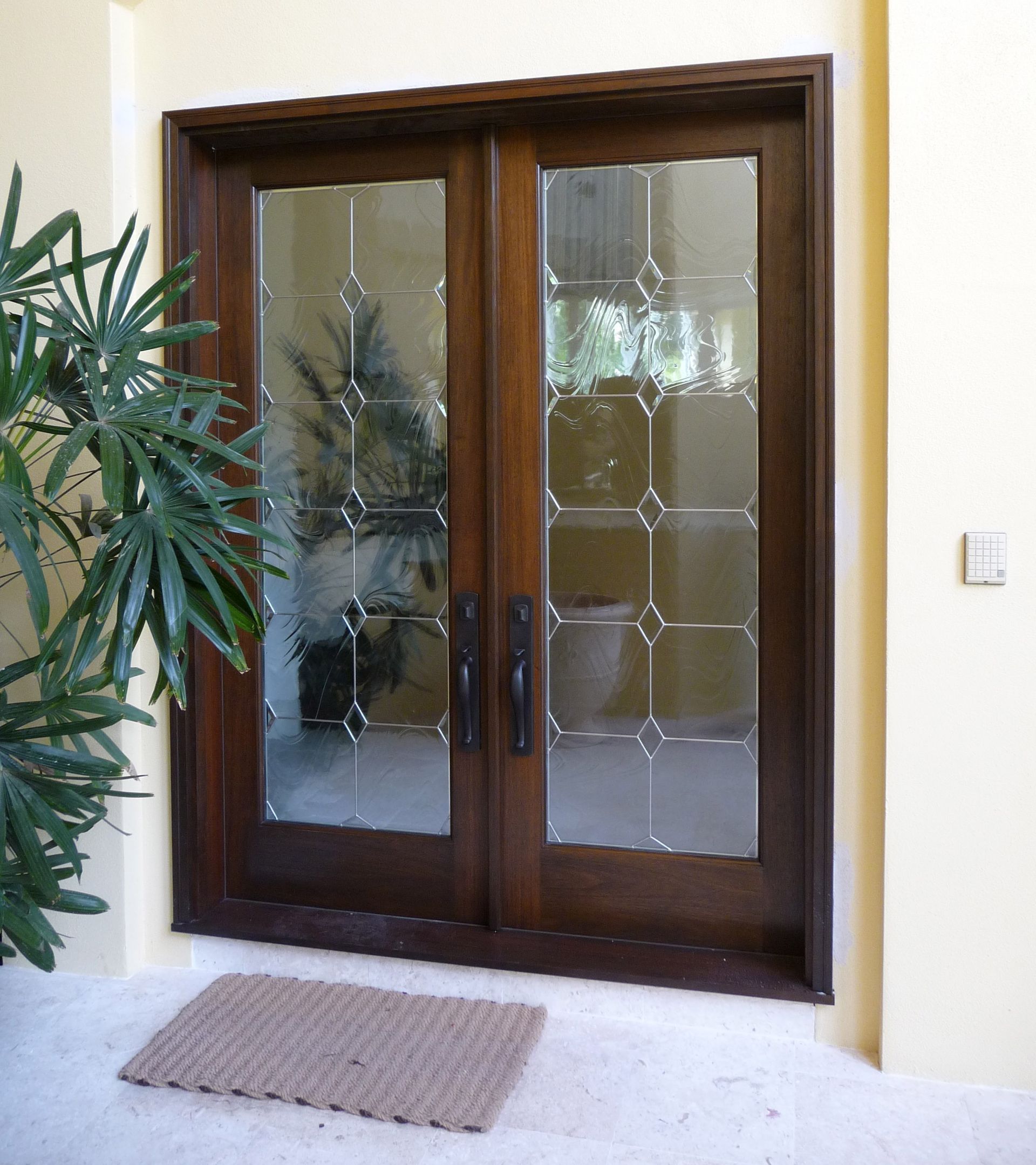 A pair of dark wood double doors with diamond-patterned glass panels, set in a light yellow entryway.