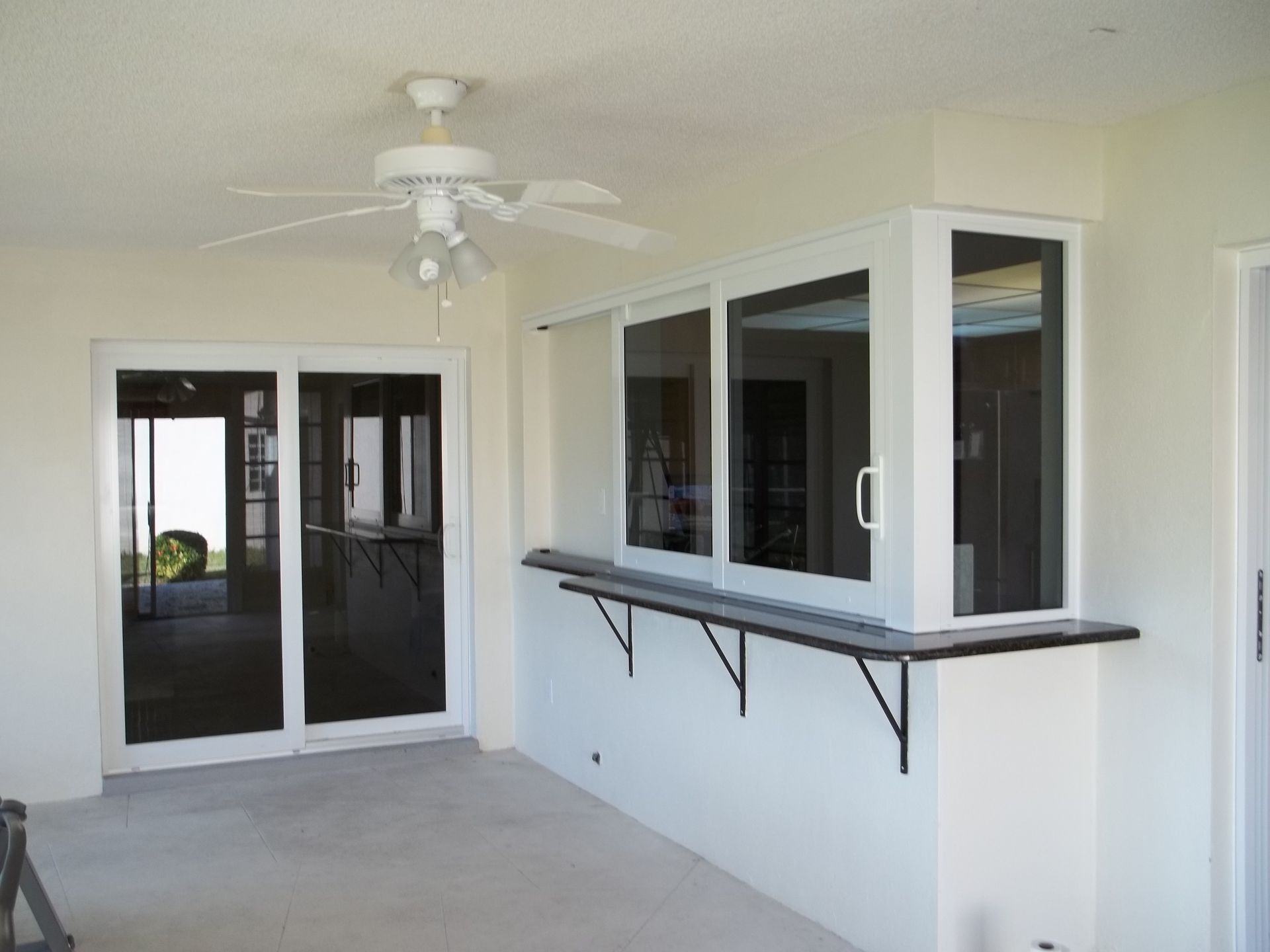 A pass-through serving window with a black counter and metal brackets installed on an outdoor patio wall.