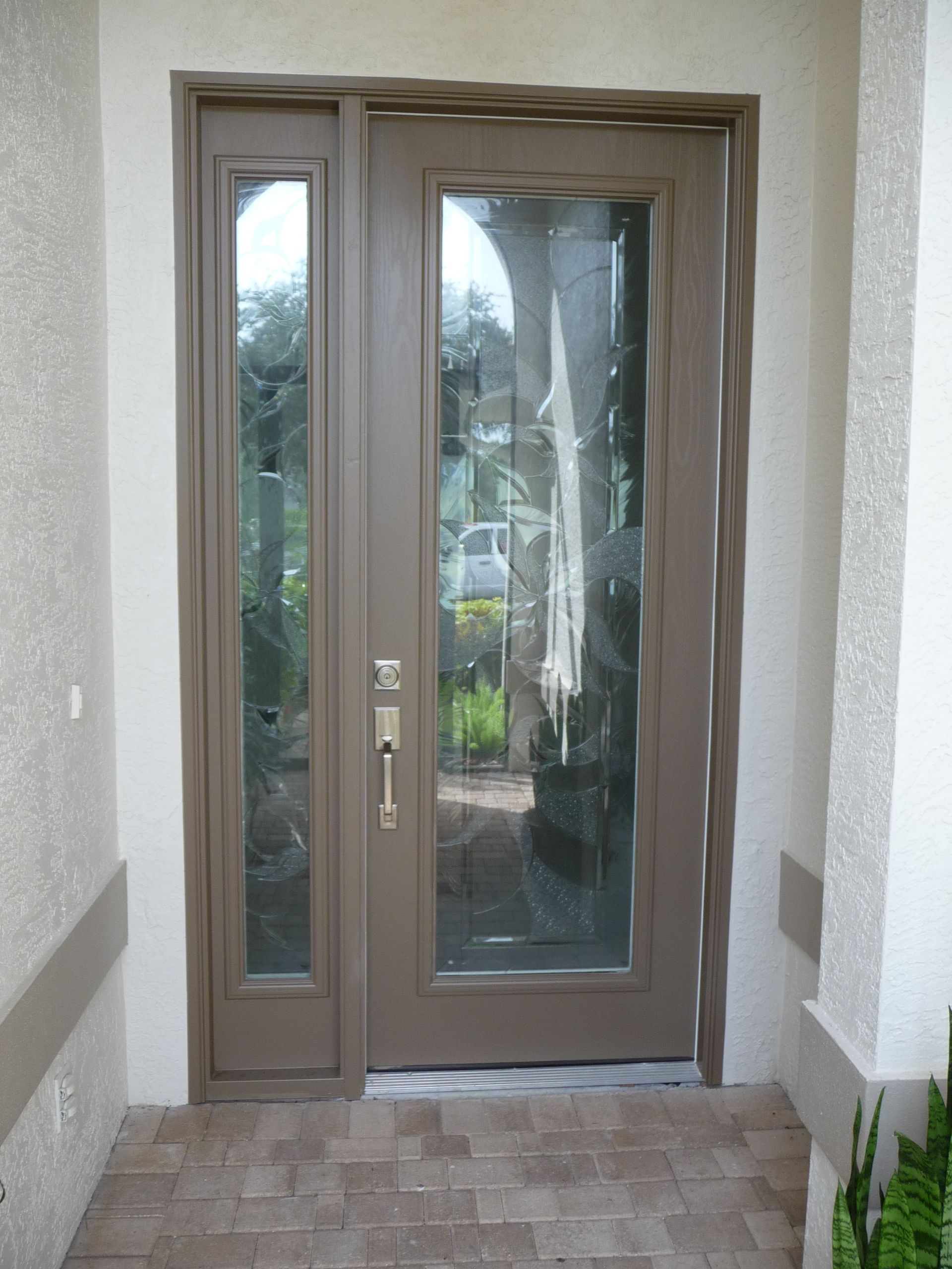 A brown front door with a matching side panel, both featuring large glass inserts, framed by a textured cream wall.