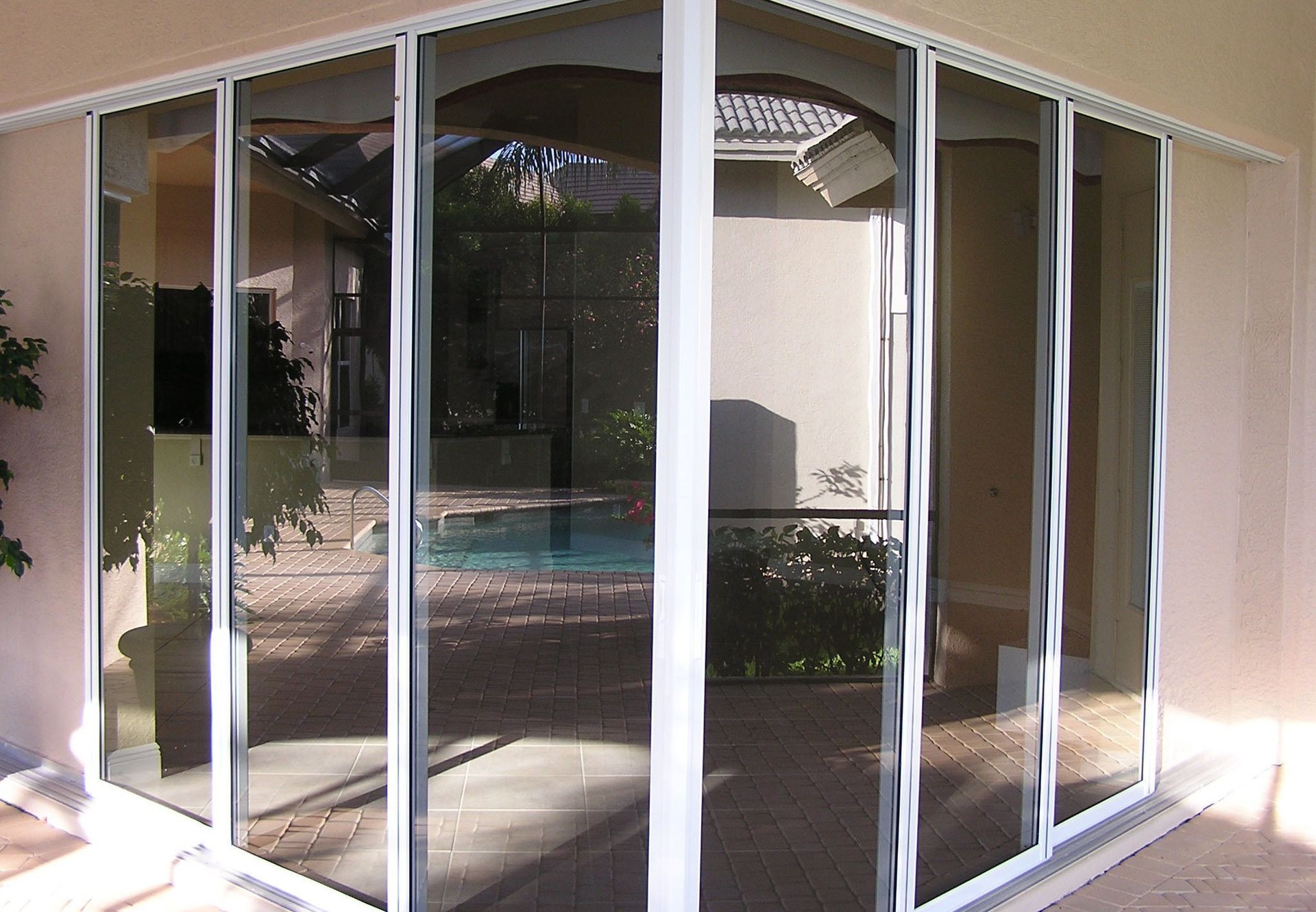 White-framed glass sliding doors reflecting a patio area with a pool and house exterior.