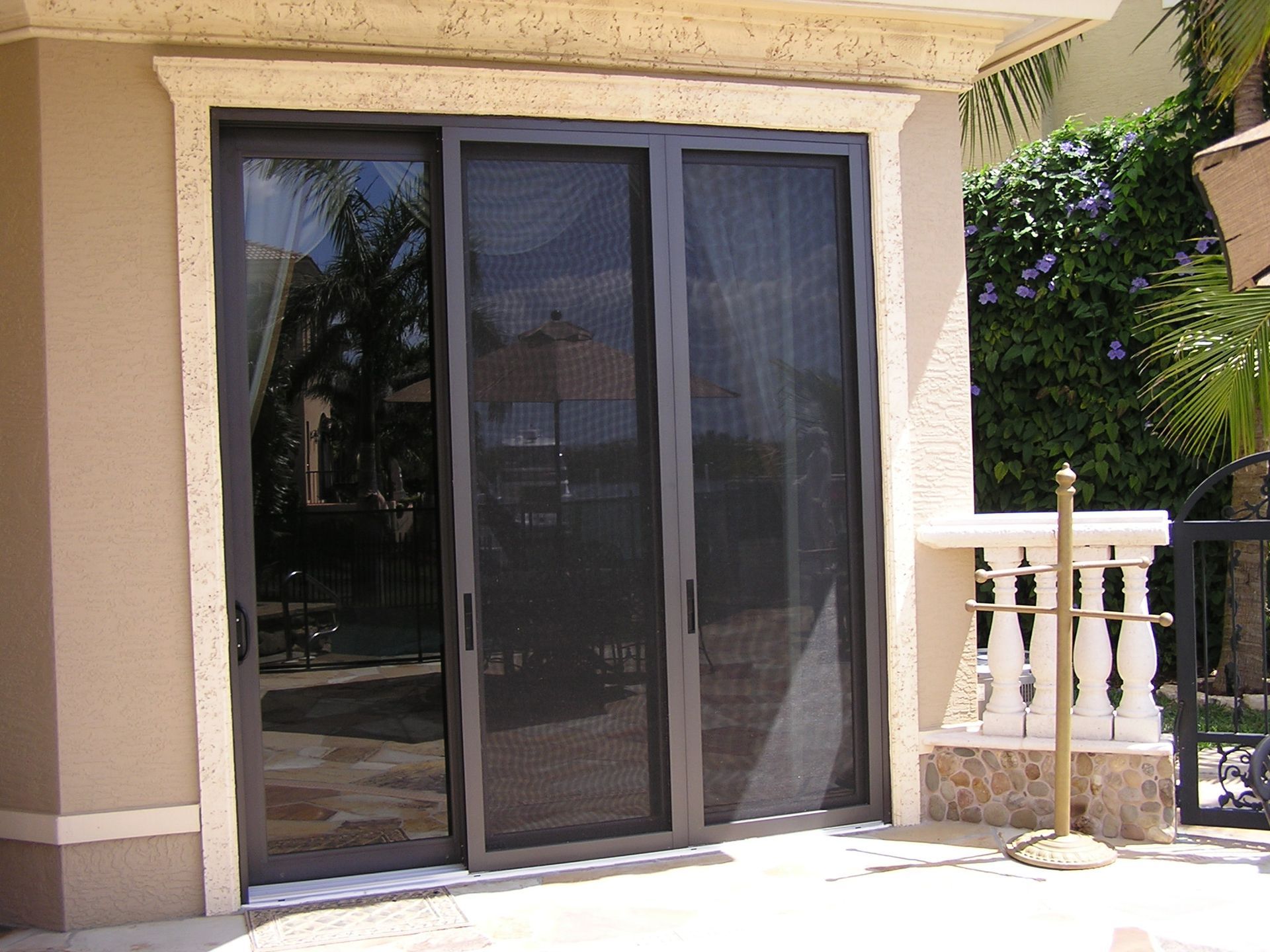 A sliding glass door with a dark screen panel, set in a beige wall with stone trim, next to a white stone railing.