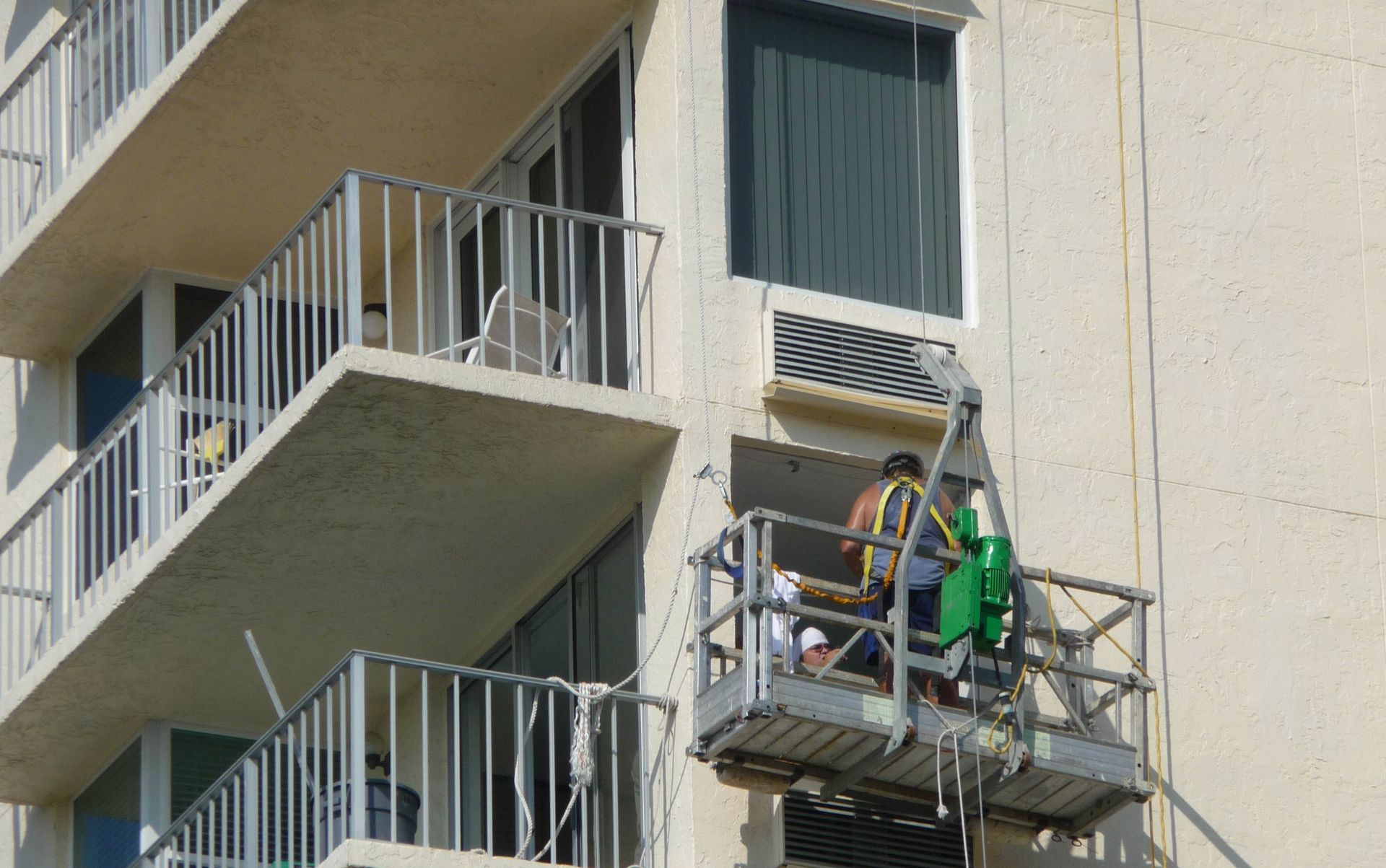Construction workers on a suspended scaffolding platform performing exterior maintenance on a high-rise building.