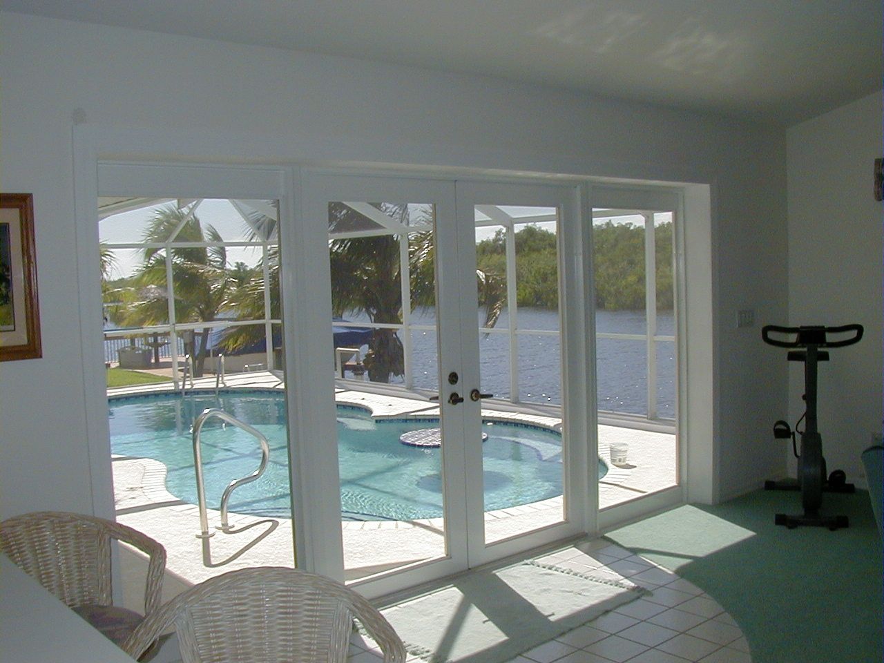 A bright indoor room with a view through glass doors to a backyard swimming pool and water view, with an exercise bike.
