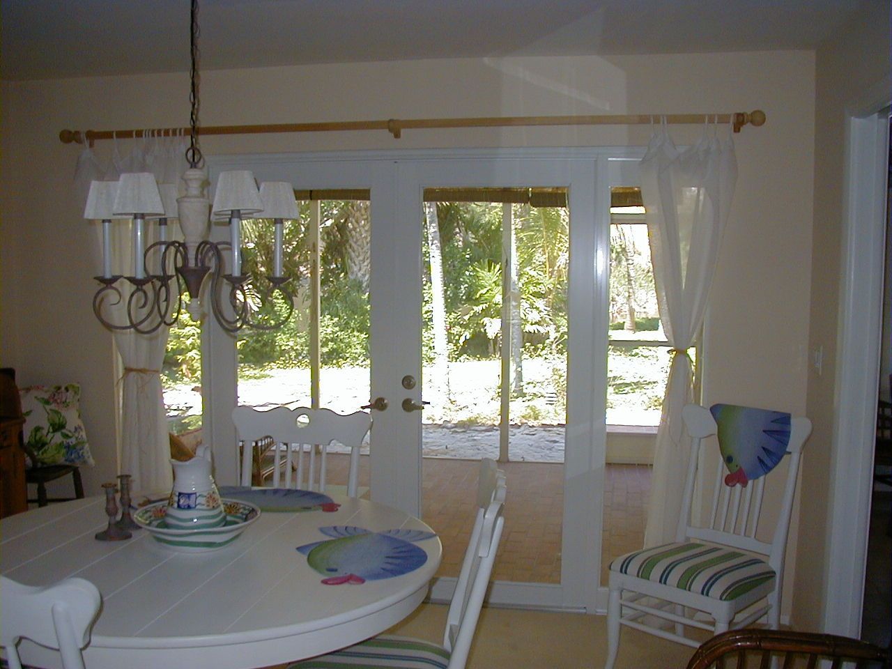 A dining area with a round white table, chandelier, and chairs positioned in front of French doors leading to a patio.