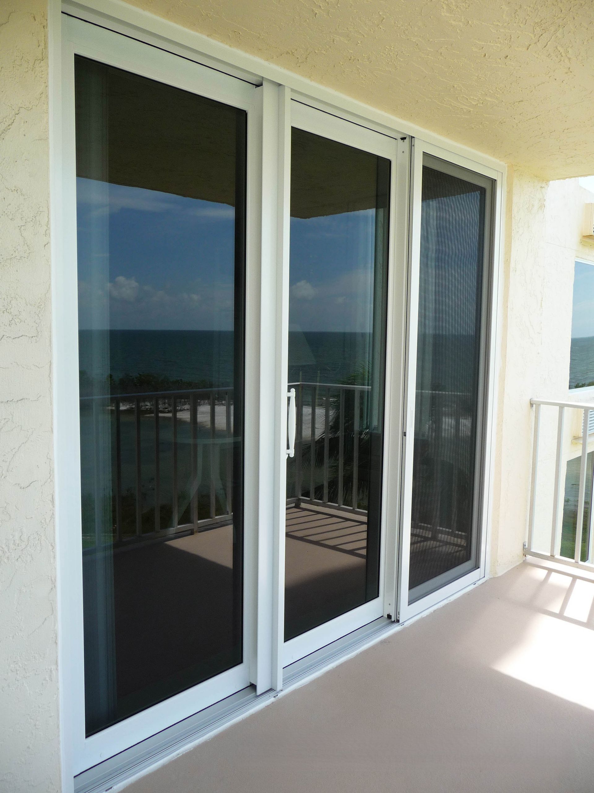 Three-panel white sliding glass door leading to a balcony with an ocean view.