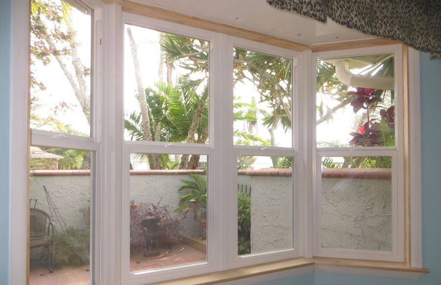 A white bay window overlooking a small patio with potted plants and a stucco wall.