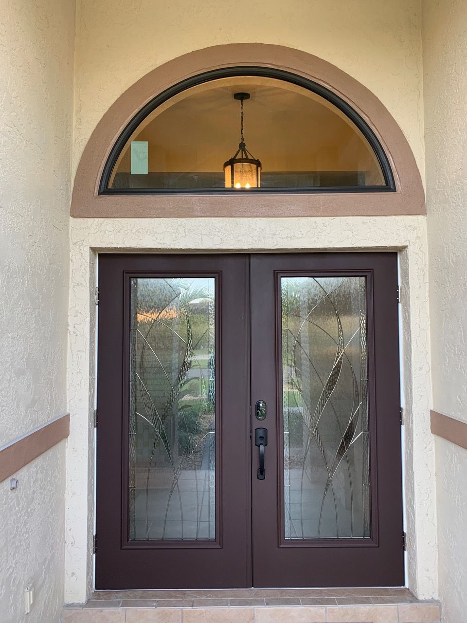 A front entryway featuring dark brown double doors with patterned glass panels and a large arched transom window above.