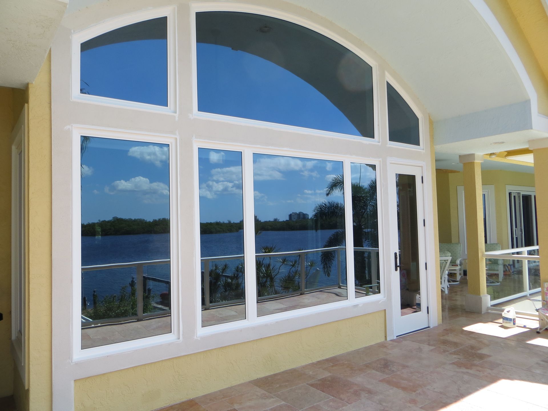 Exterior view of a large, arched multi-pane window and a glass door on a house patio overlooking a lake.