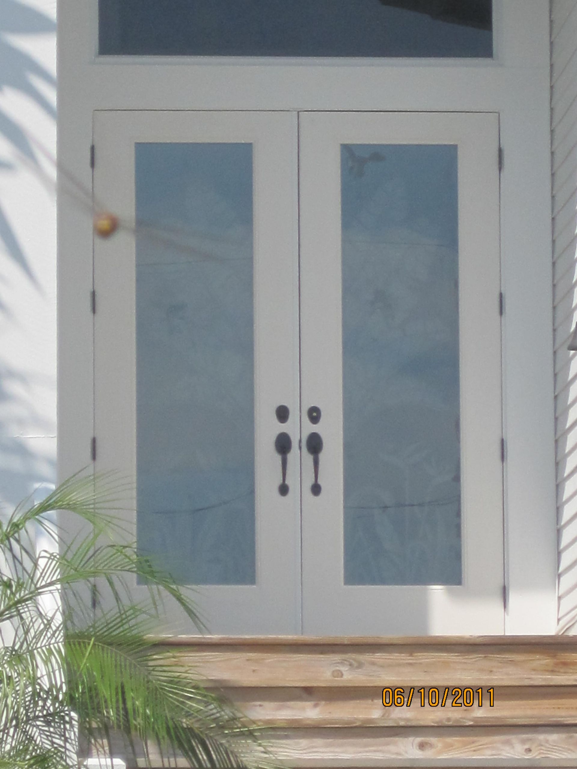 A white double door with rectangular glass inserts, black handles, and a transom window above, set atop wooden steps.