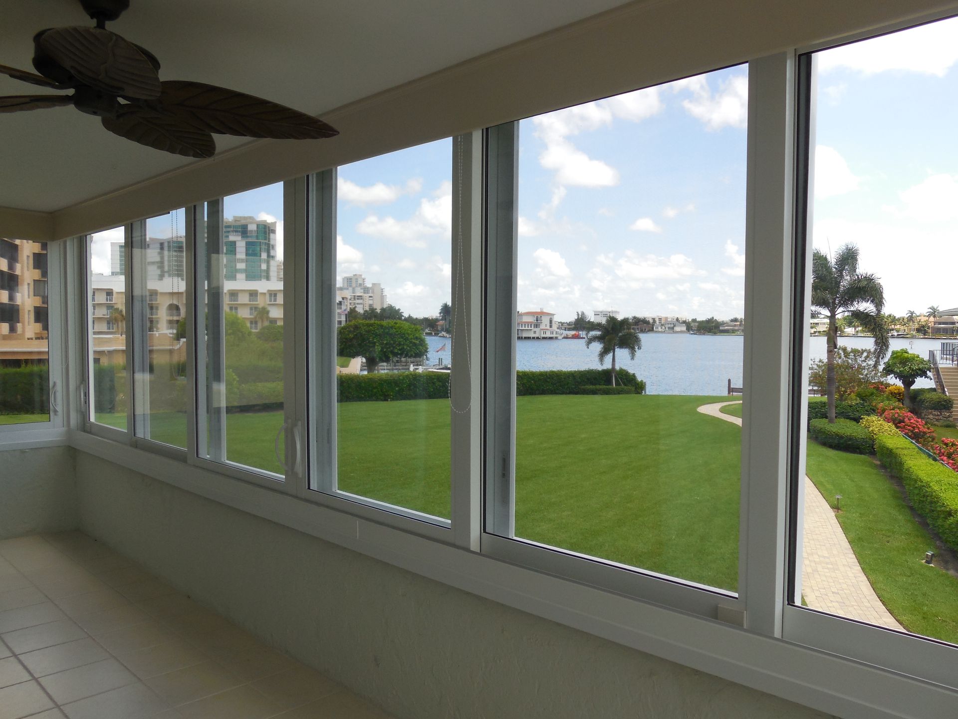 A view from a covered patio through large sliding glass doors looking out over a green lawn and a calm bay.