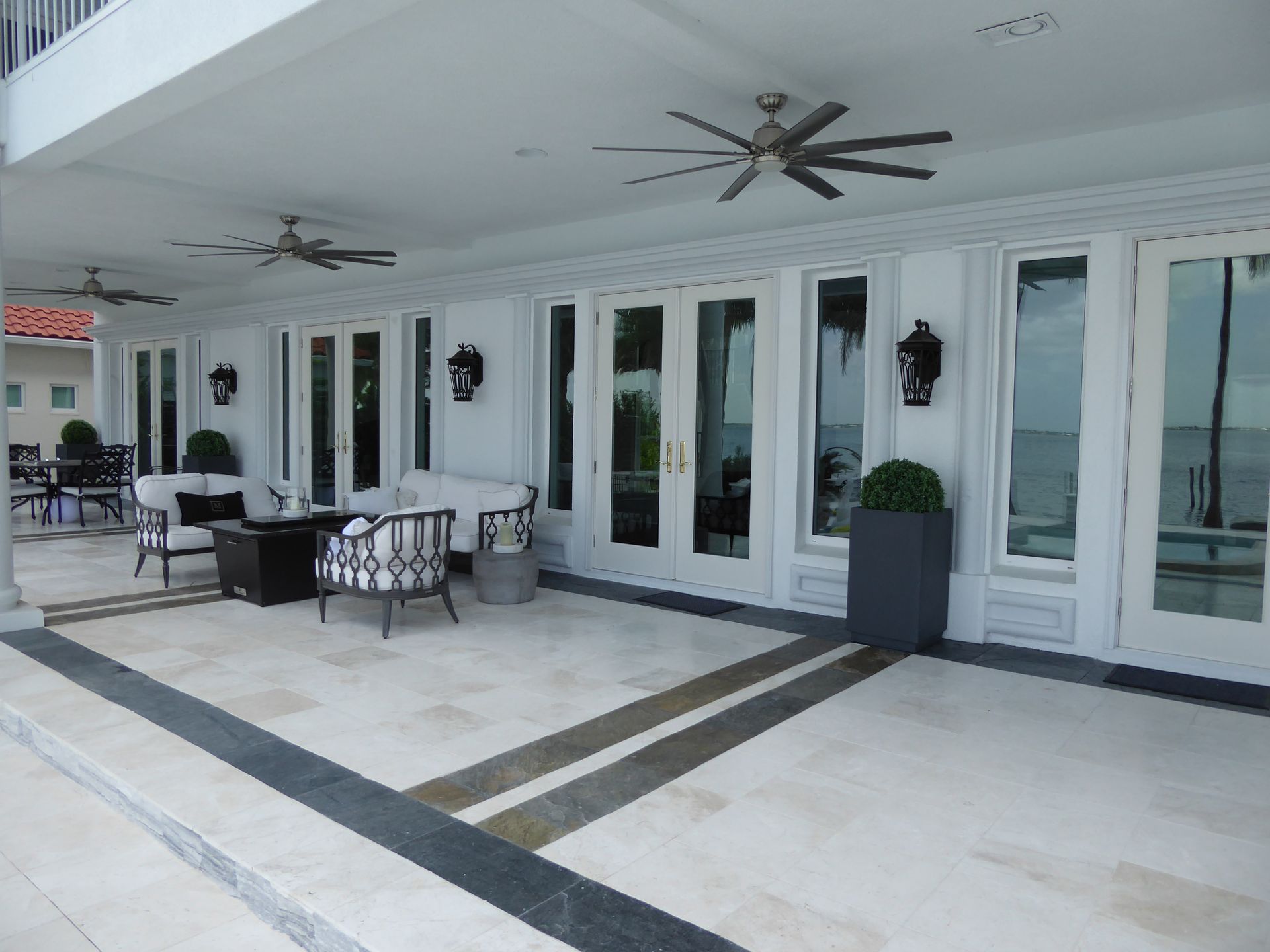 A spacious, covered outdoor patio with light-colored tile floors, cushioned seating, and ceiling fans.