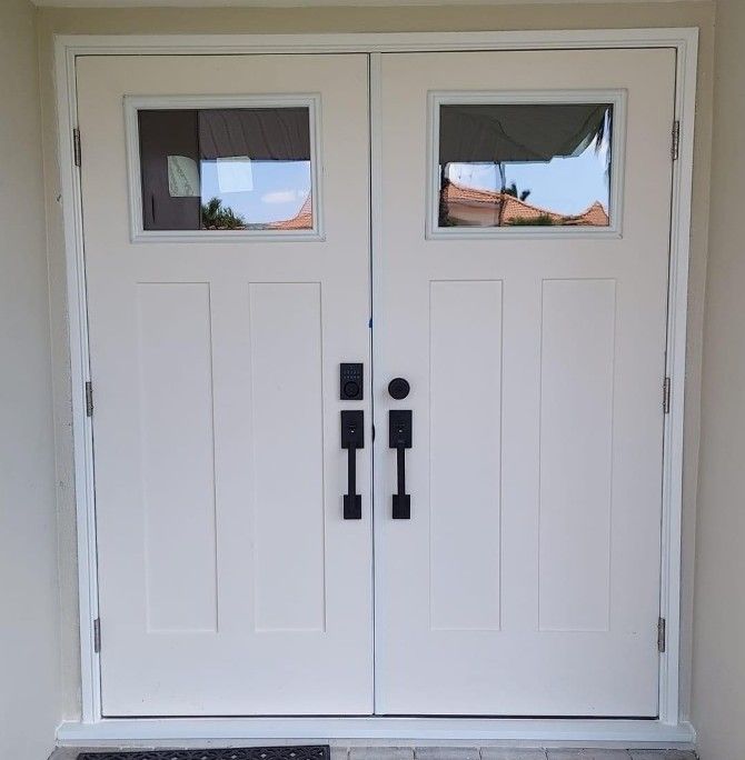 A pair of white double front doors with rectangular windows, two black rectangular door handles, and a smart lock.