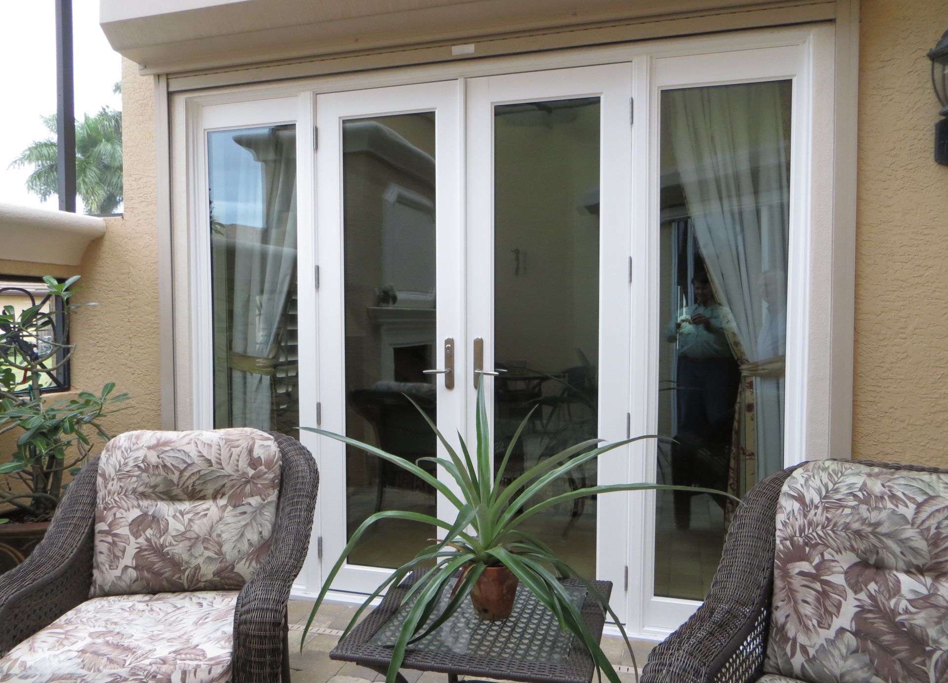 Modern home exterior entrance with a wood door, stone columns, large windows reflecting a sunset, and potted plants.