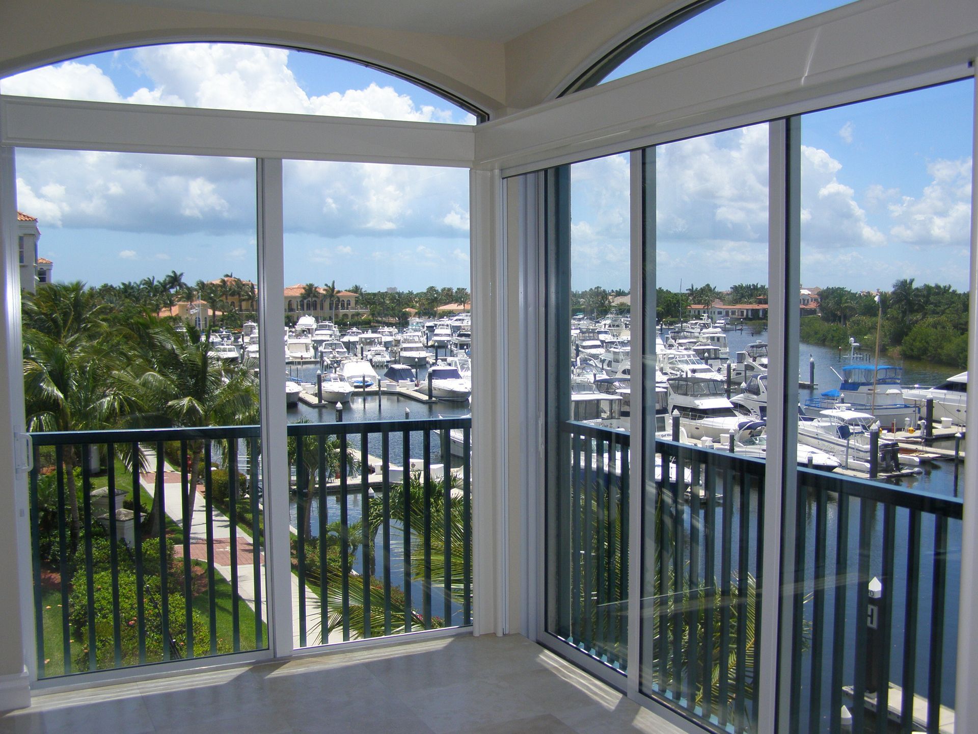 View from a balcony overlooking a marina with boats, water, and palm trees under a blue sky.
