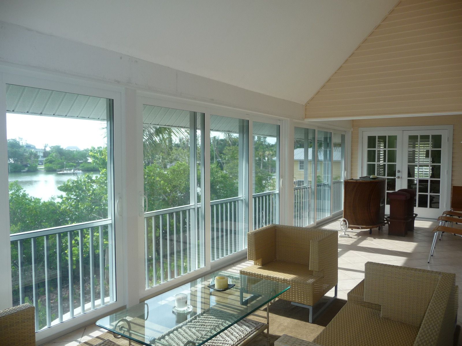 Bright sunroom with glass walls, wicker chairs, and a lake view beyond the balcony.
