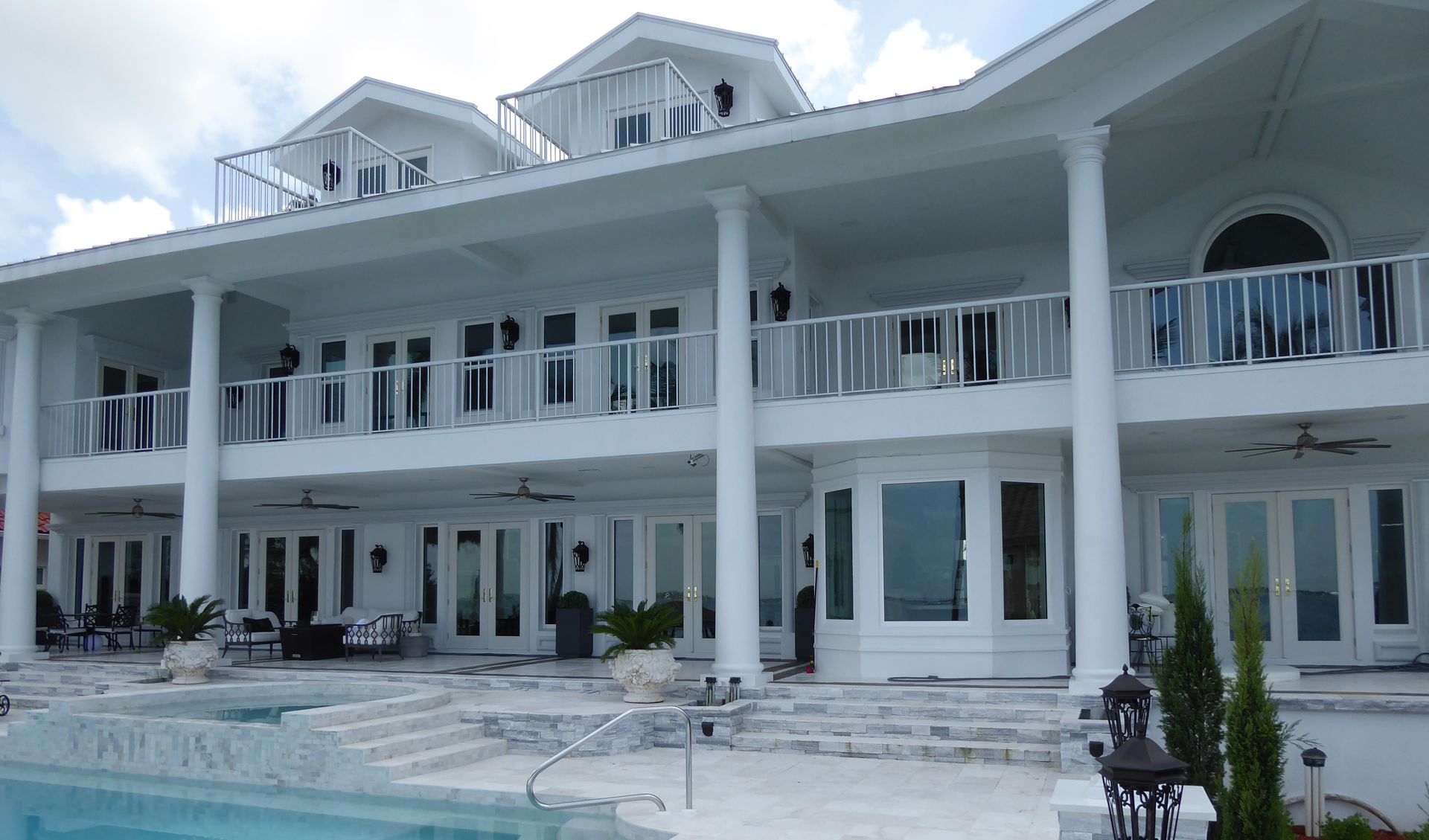 Large white luxury mansion with columns, balconies, and a swimming pool in front