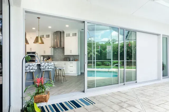 Modern kitchen opening to a patio with sliding glass doors and a pool view.