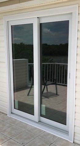 White-framed sliding glass patio door reflecting a deck railing and chair outside