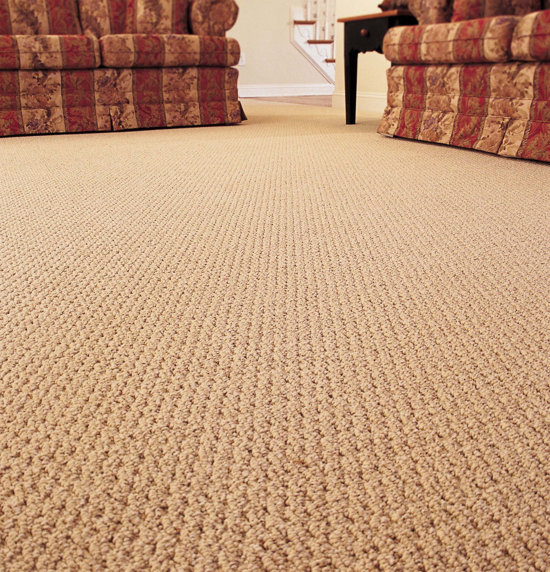 Beige carpet in a room with two patterned armchairs and a table.