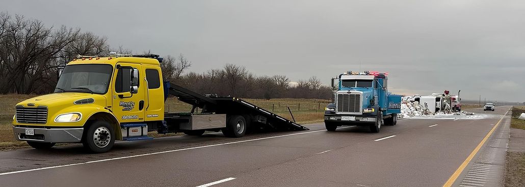 Yellow truck and blue tow truck on a highway beside a crashed vehicle in the median