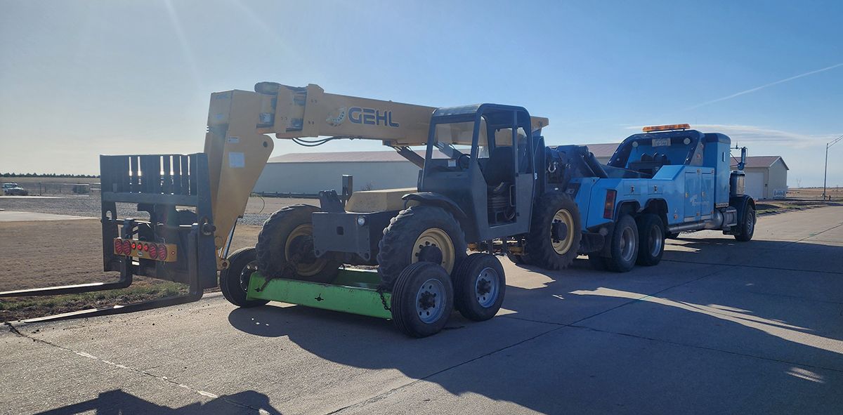 Construction equipment and a blue tow truck on a road in a barren landscape.