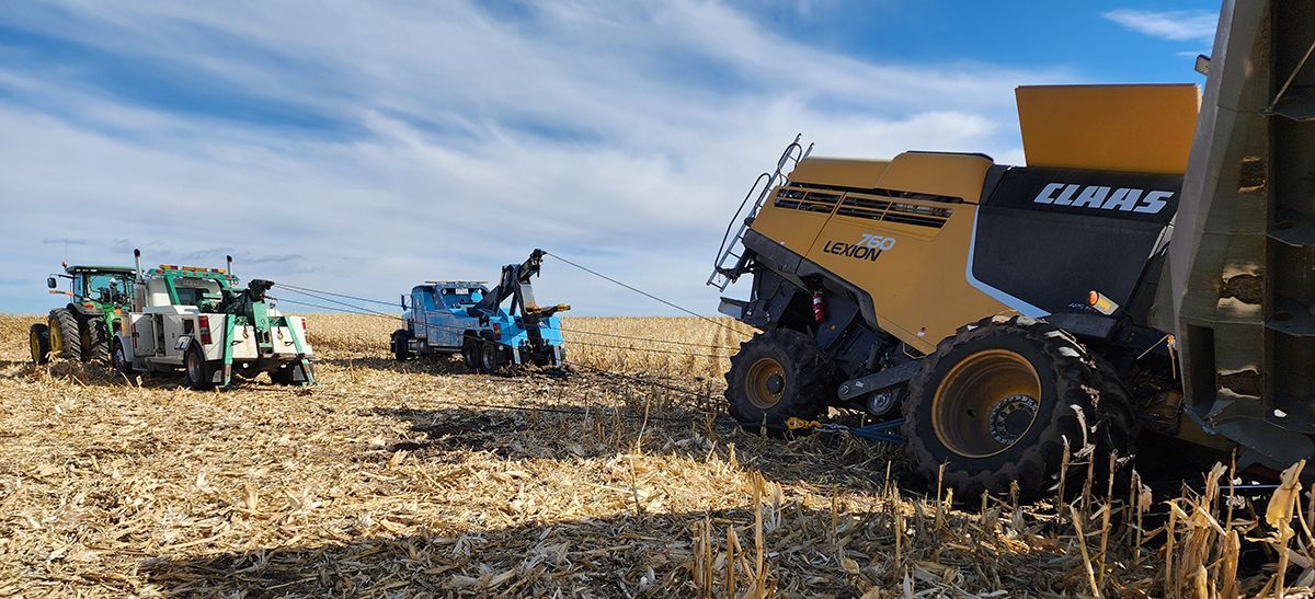 Farm machinery harvesting corn in a field, with a large combine on the right and tractors in the distance