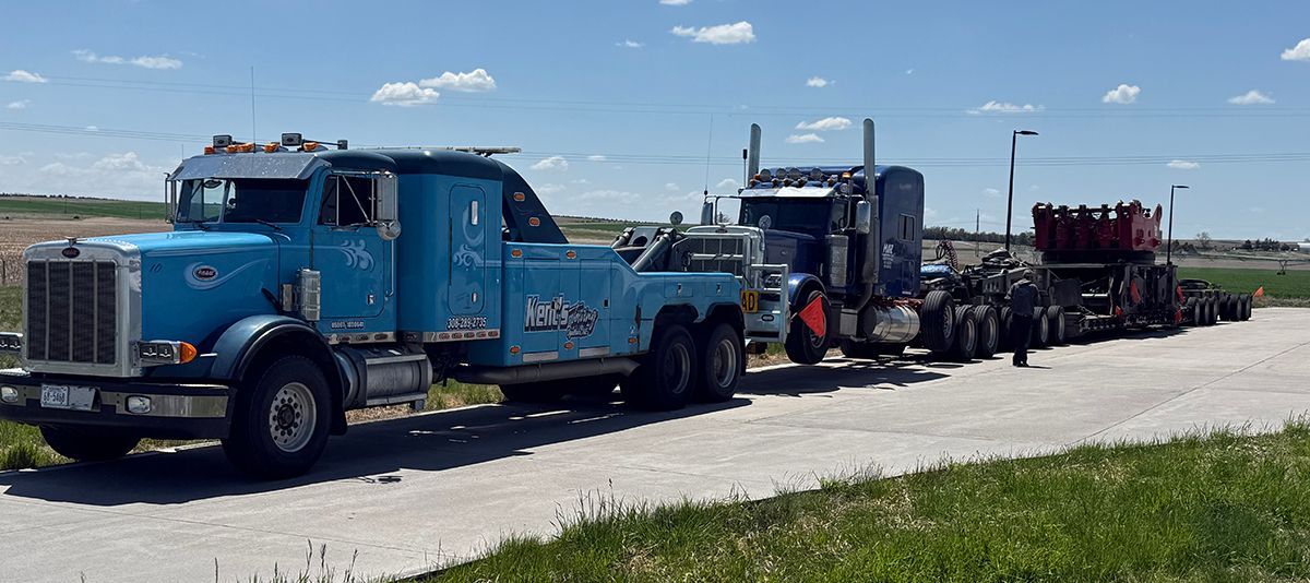 Blue semi-truck hauling a flatbed trailer with construction equipment on a sunny roadside