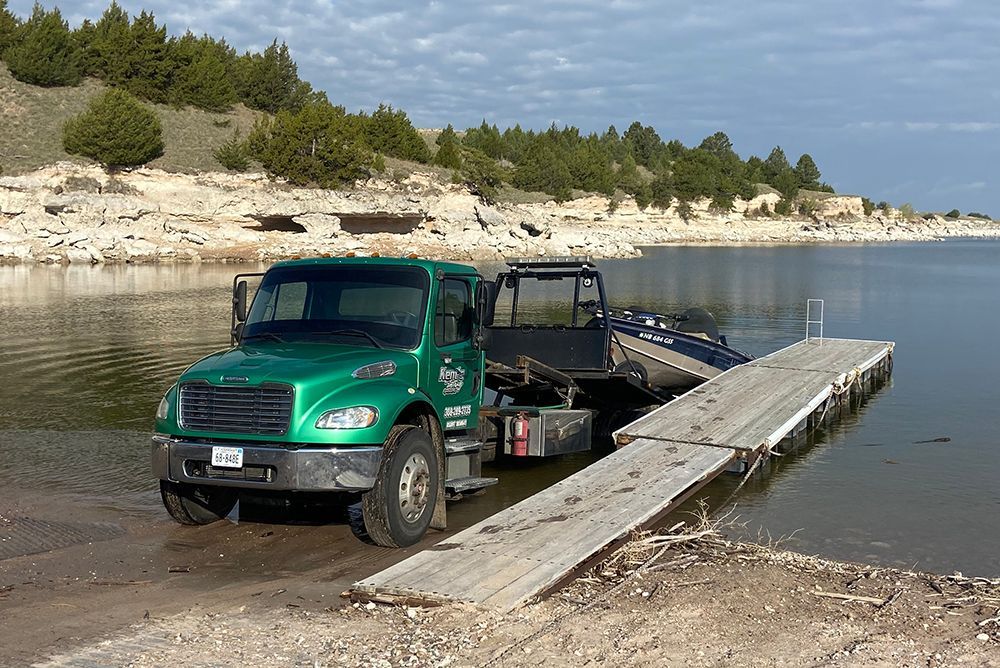 Green truck and trailer launching a boat on a ramp at a calm lakeshore