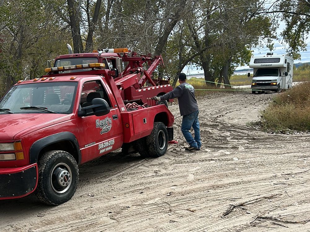 Red tow truck with operator loading a white truck on a muddy roadside