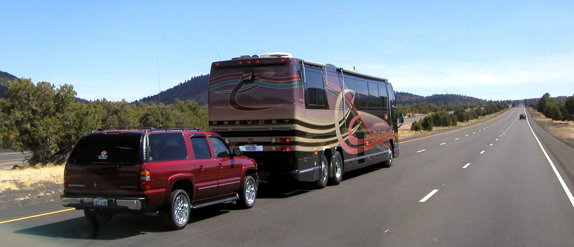 Red SUV towing a large RV on a highway beside a mountainous landscape