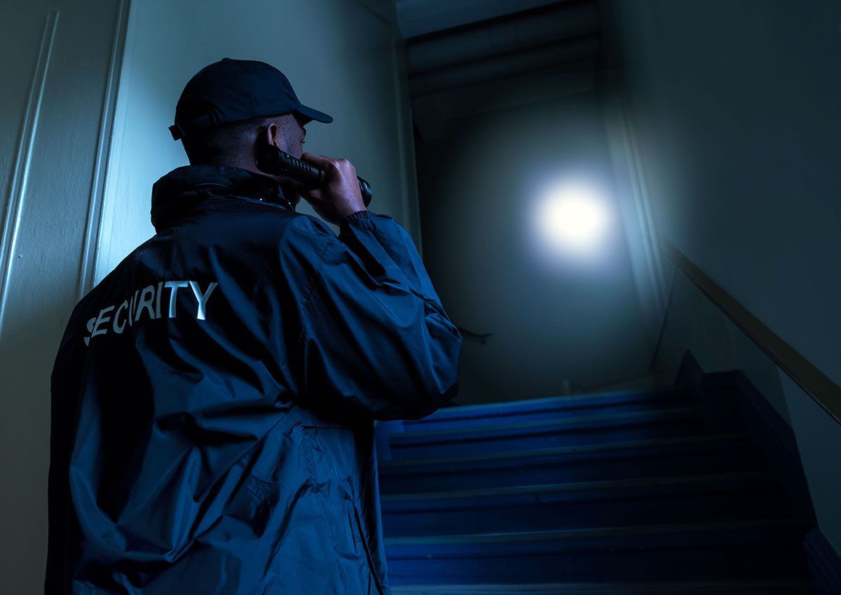 Security guard ascending dim stairs with flashlight, scanning a dark hallway
