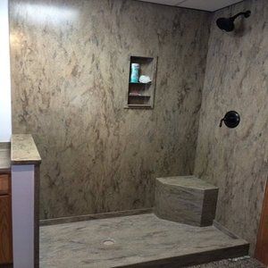 A bathroom with a walk in shower with marble walls and a bench.