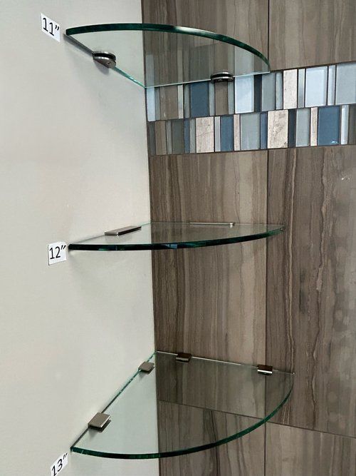 Three glass shelves are lined up on a wall in a bathroom.