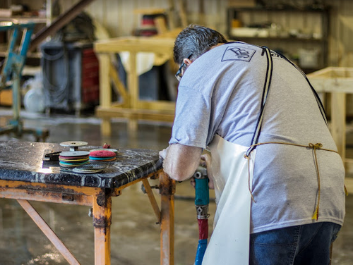 A man in an apron is working on a table in a workshop.
