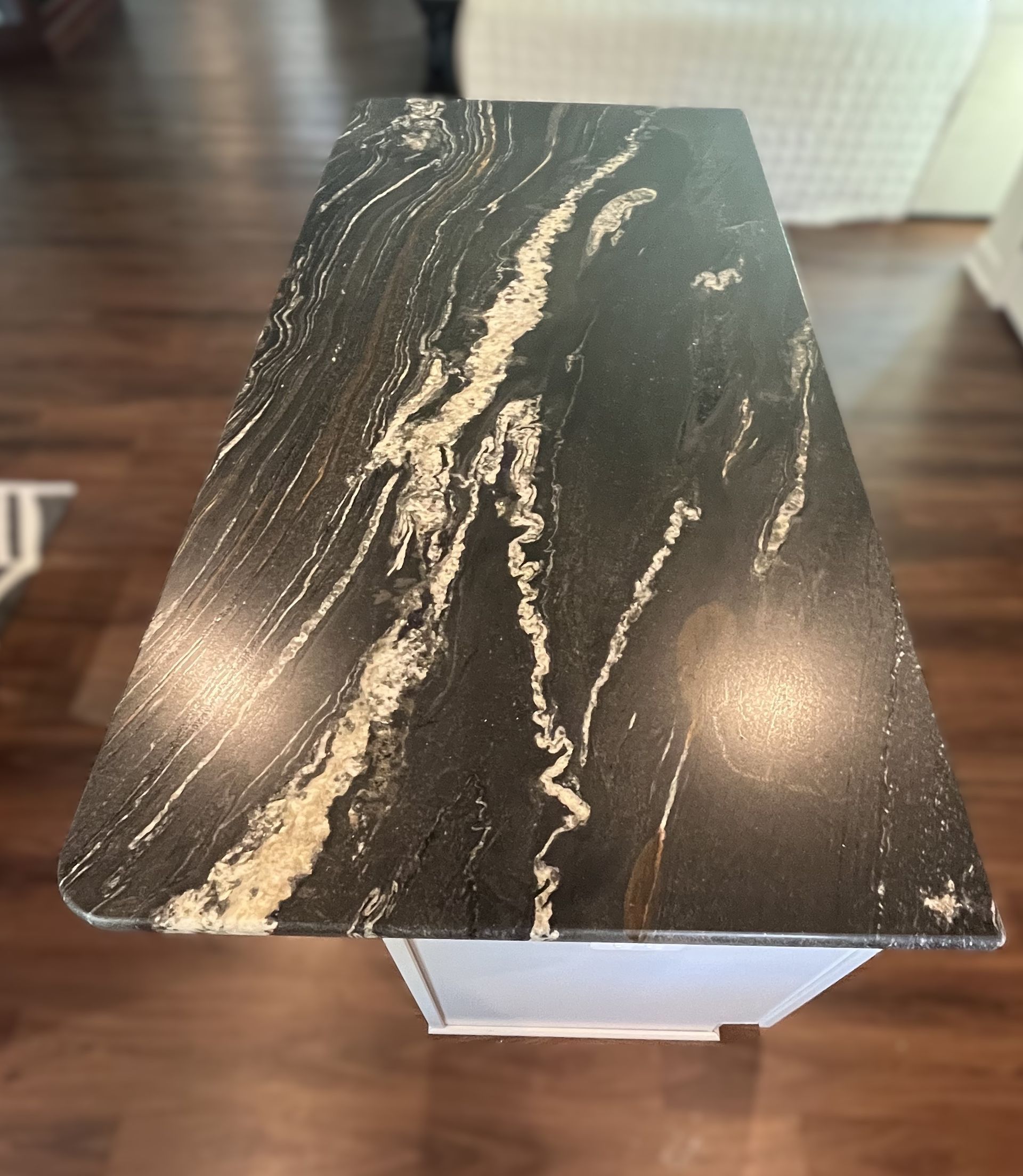 Dark countertop with white and gold veining sits atop a white cabinet, with a dark wood floor in the background.