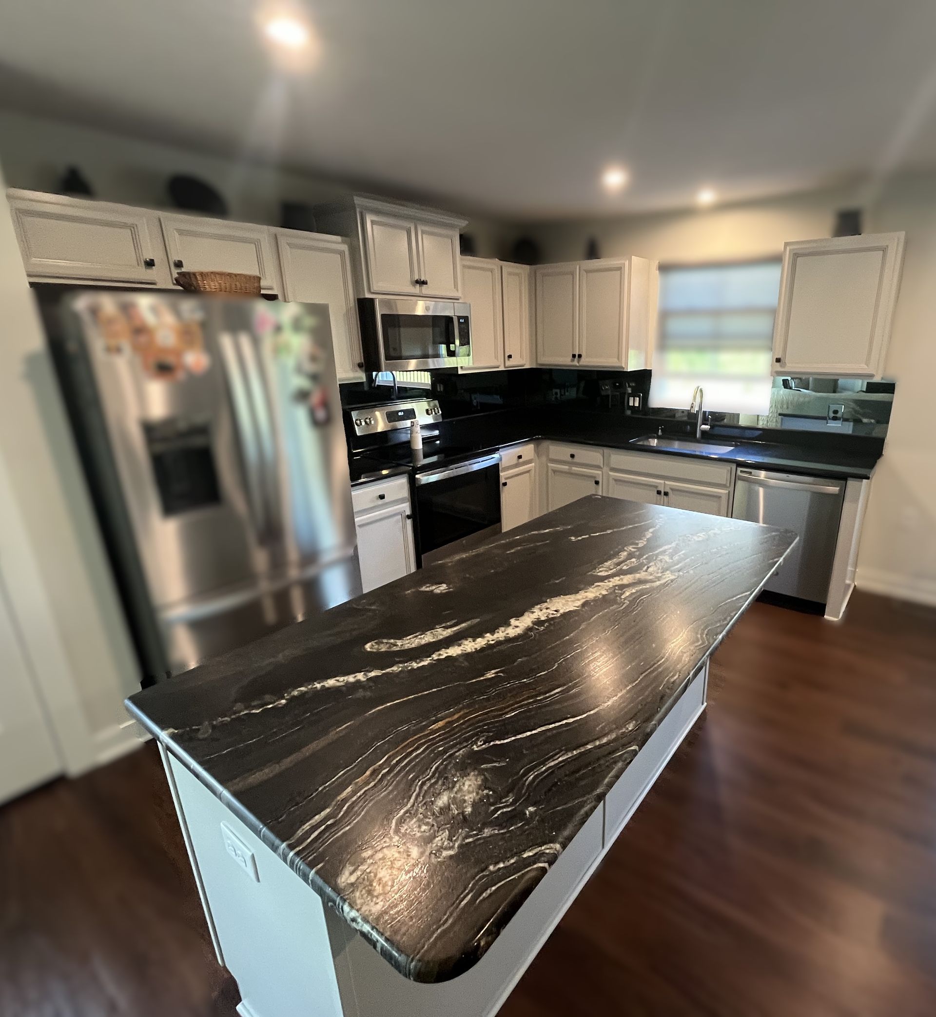 Kitchen with black granite countertops, white cabinets, stainless steel appliances, and dark wooden floors.