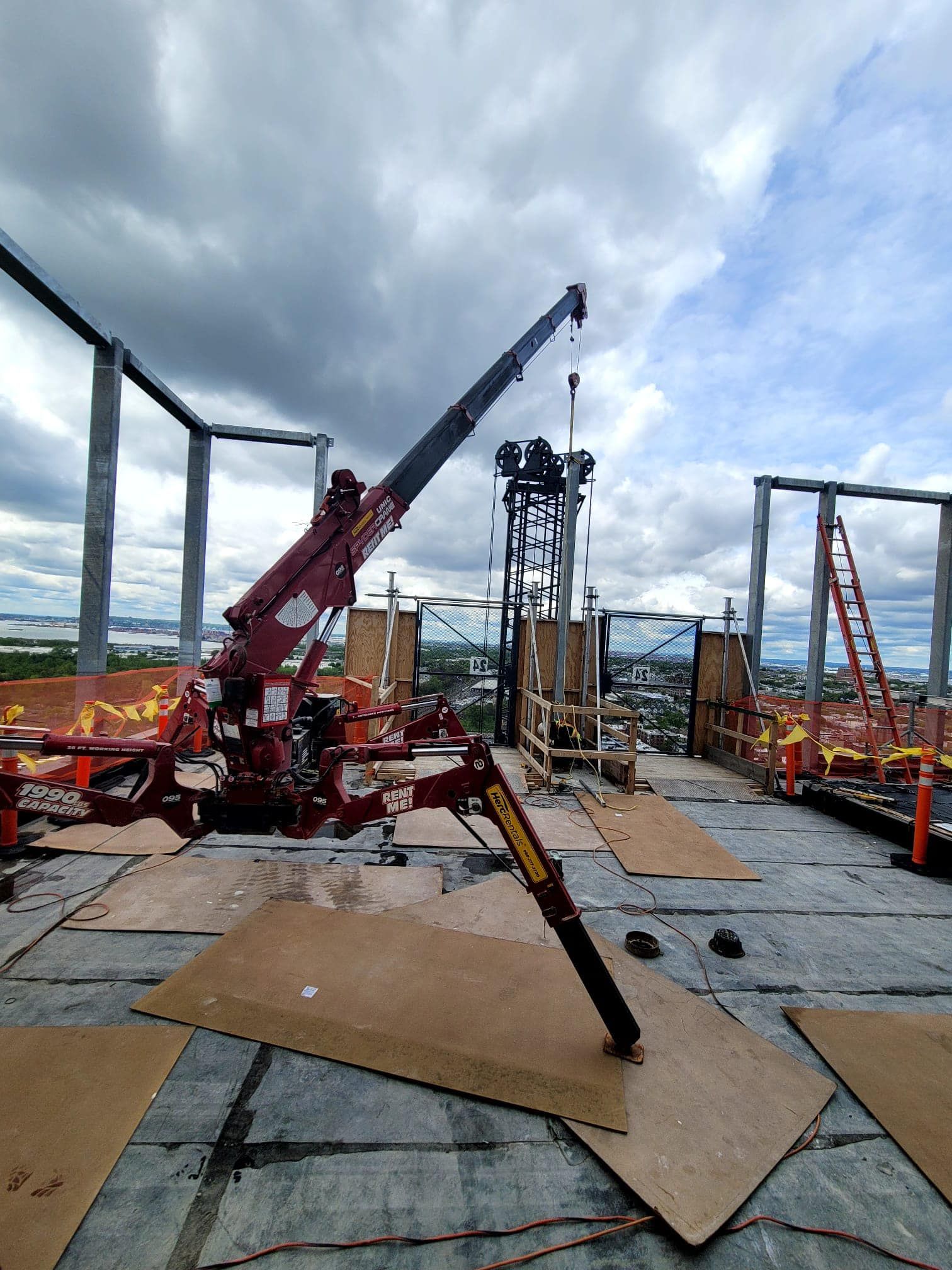 A red crane is sitting on top of a building under construction.