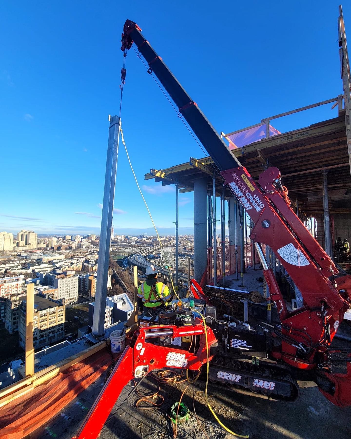 A red crane is being used to lift a pole on top of a building.