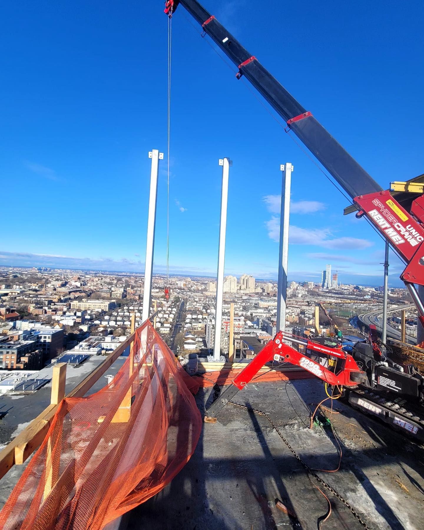 A red and black crane is on top of a building with a city in the background