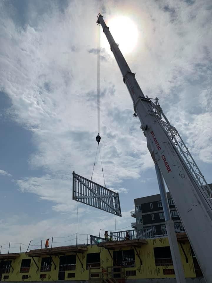 A large crane is lifting a piece of metal on top of a building.
