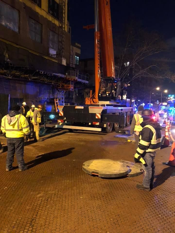 A group of construction workers are standing around a manhole cover.