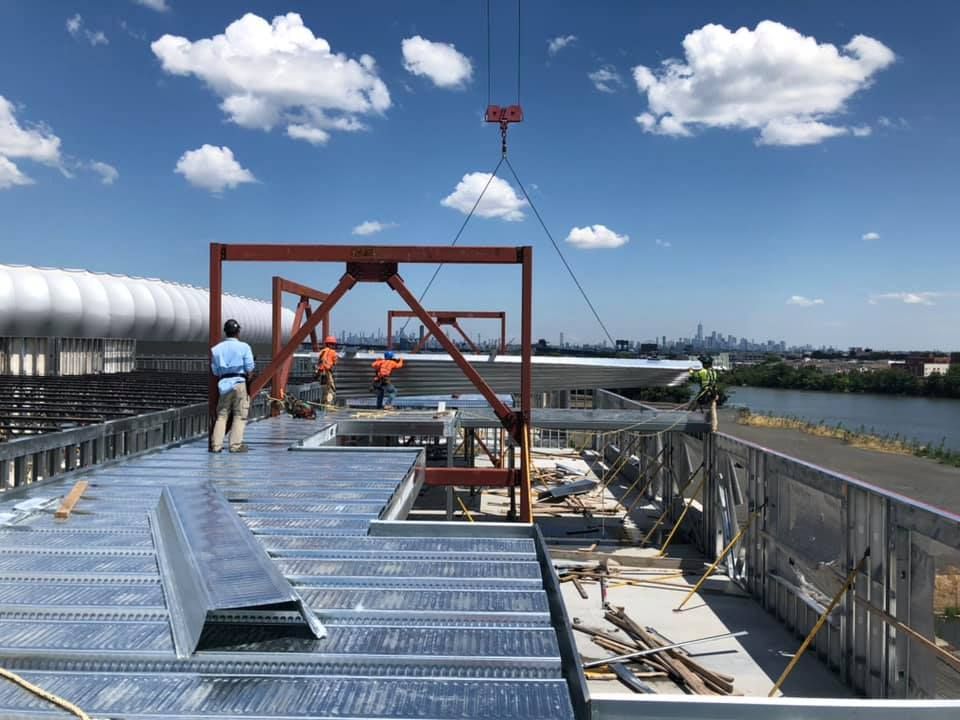 A crane is lifting a metal structure on top of a building under construction.