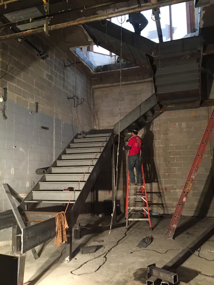 A man is standing on a ladder in front of a staircase under construction.