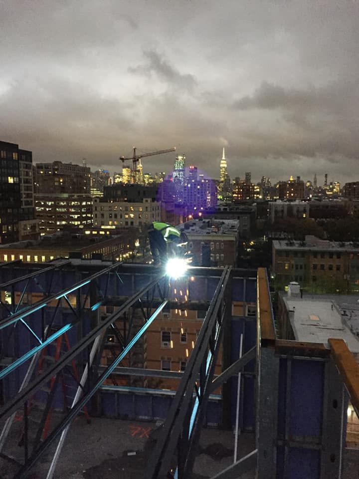 A man is welding on top of a building at night