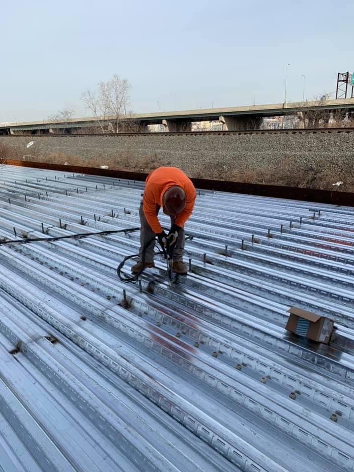 A man in an orange shirt is working on a metal roof.